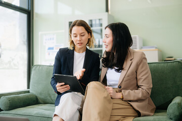 Fototapeta premium Two businesswomen strategizing with a tablet in a professional office. Highlight teamwork, leadership,