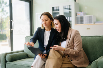 Two businesswomen collaborate using a tablet in a stylish office setting. Perfect for concepts