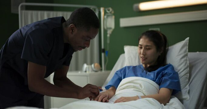 In a hospital room, a young African doctor puts a catheter on a woman injured in a car accident.