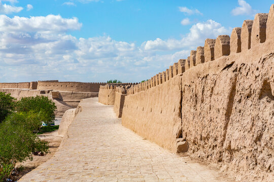 Itchan Kala citadel defensive walls, featuring mud-brick construction, a paved walkway, and greenery under a blue sky. Khiva, Uzbekistan