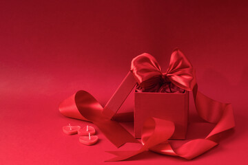 Red gift box with satin ribbon and heart-shaped candles on red background. Mockup of greeting card for Valentine's Day, birthday.