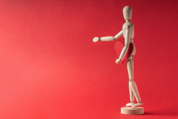 Wooden model of a man holding a wooden heart figurine on a red background. Mockup, banner for Valentine's Day, Birthday.