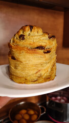 Hand gripping ceramic plate with golden braided easter bread, sprinkled raisins, colorful eggs nestled in background pottery