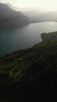 Vertical drone shot of beautiful glacial emerald-green lake surrounded by lush forests, natural lake in summer afternoon under clear blue sky