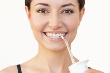 Close-up young pretty Caucasian brunette woman brushing her teeth with a white portable irrigator...