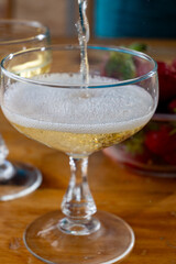Pouring of brut champagne bubbles wine in coupe glasses and small bowl with fresh strawberries