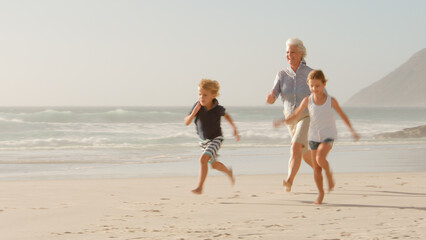 Grandmother Chasing Grandchildren Along Beach On Summer Vacation