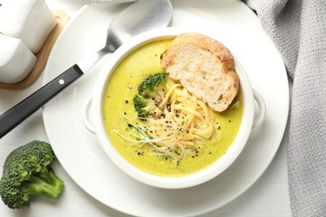Delicious broccoli cream soup served on white wooden table, flat lay