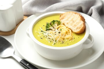 Delicious broccoli cream soup served on white table, closeup