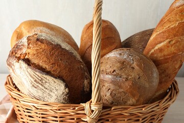 Different freshly baked bread loafs in wicker basket on table, closeup