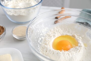 Making cinnamon rolls. Flour with egg yolk in bowl and other ingredients for dough on white table, closeup