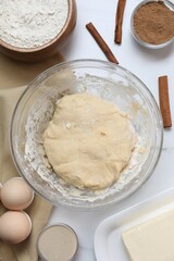 Making cinnamon rolls. Fresh dough in bowl and ingredients on white table, flat lay