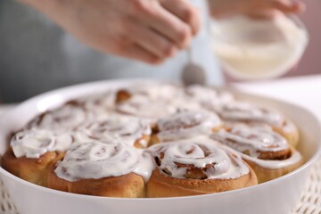 Delicious frosted cinnamon rolls and woman at table, selective focus