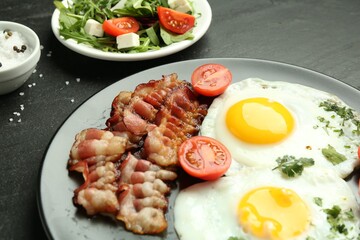 Tasty brunch. Delicious fried eggs, bacon and salad served on black table, closeup
