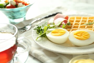 Tasty brunch. Boiled egg, Belgian waffle, arugula and ham on light table, closeup