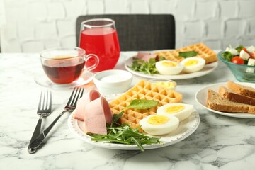 Tasty brunch. Boiled egg, Belgian waffle, arugula and ham on white marble table