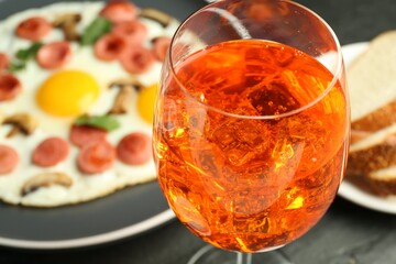 Tasty brunch. Aperol cocktail, delicious fried eggs with sausage served on black table, closeup