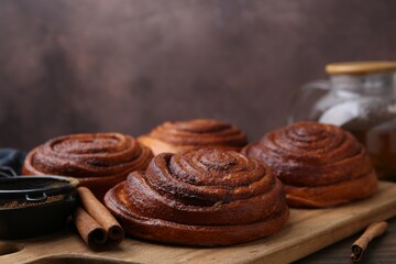 Delicious cinnamon rolls on wooden table against brown background, closeup
