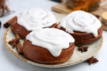 Tasty cinnamon rolls with cream and spices on white tiled table, closeup