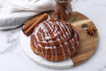 Tasty cinnamon roll with cream and spices on white marble table, closeup