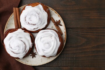 Tasty cinnamon rolls with cream and spices on wooden table, top view. Space for text