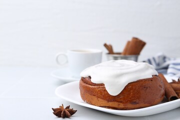 Tasty cinnamon roll with cream and spices on white table, closeup. Space for text