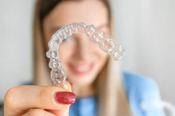 Women hand hold invisalign braces, transparent aligner, invisible retainer or orthodontic silicone trainer with blur mile in background. A way to have a beautiful smile.