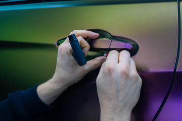 A specialist in wrapping a car with chameleon-colored vinyl film in the process of work. Car...