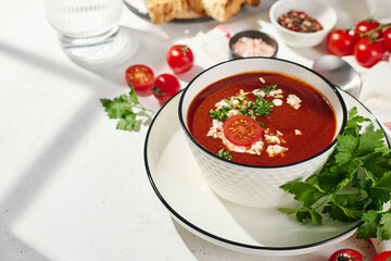 Spanish Cold Tomato Gazpacho Soup garnished with parsley, feta cheese and spices with toasted bread slices, tomatoes and herbs on white table