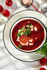 Spanish Cold Tomato Gazpacho Soup garnished with parsley, feta cheese and spices with toasted bread slices, tomatoes and herbs on white table