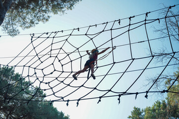 Little girl bravely walks on the rope web in adventure park. Safe climbing with helmet and insurance. Child in adventure park in forest, extreme sport © Nadezda Anokhina