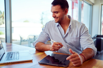 Young businessman using stylus pen on digital tablet while working on laptop in bright modern office