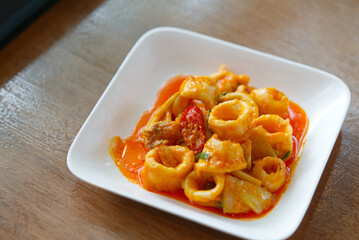 Stir-fried squids with salty egg yolks on wooden table in a restaurant with natural light from window, close up Thai food menu.