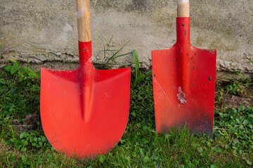 Red shovels resting against a gray wall in a grassy garden