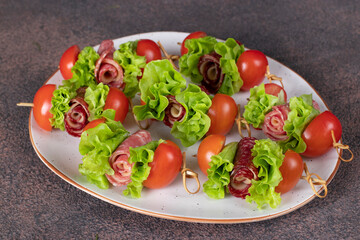 Canape with sausage, cheese, cherry tomatoes and lettuce leaves on white plate