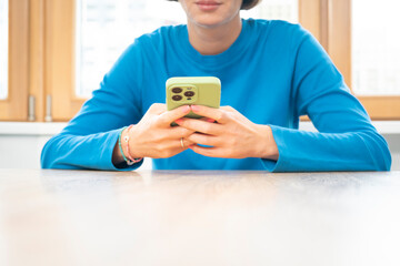 A young girl sits at the table and texts on the phone	