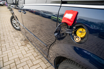 Nahaufnahme eines geöffneten Tankdeckels eines Fahrzeugs mit einem gelben Benzinverschluss und einem LPG (Autogas) Adapter. Ein rotes Täschchen mit der Aufschrift „GAS EQUIPMENT“ ist am Tankdeckel bef