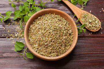 Dried oregano in bowl, spoon and green leaves on wooden table, top view