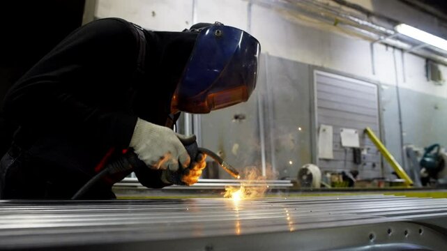 The man works as a welder at the factory. He is dressed in special clothes. High quality 4k footage