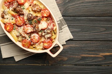 Delicious pasta casserole with cheese, tomatoes, minced meat and thyme in baking dish on wooden table, top view. Space for text