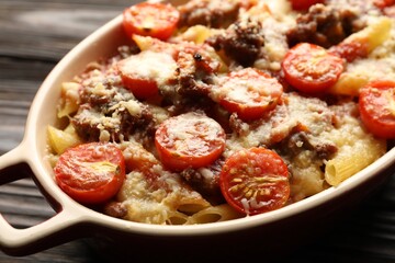 Delicious pasta casserole with cheese, tomatoes and minced meat in baking dish on wooden table, closeup