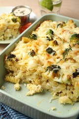 Tasty pasta casserole with cheese and broccoli in baking dish on wooden table, closeup