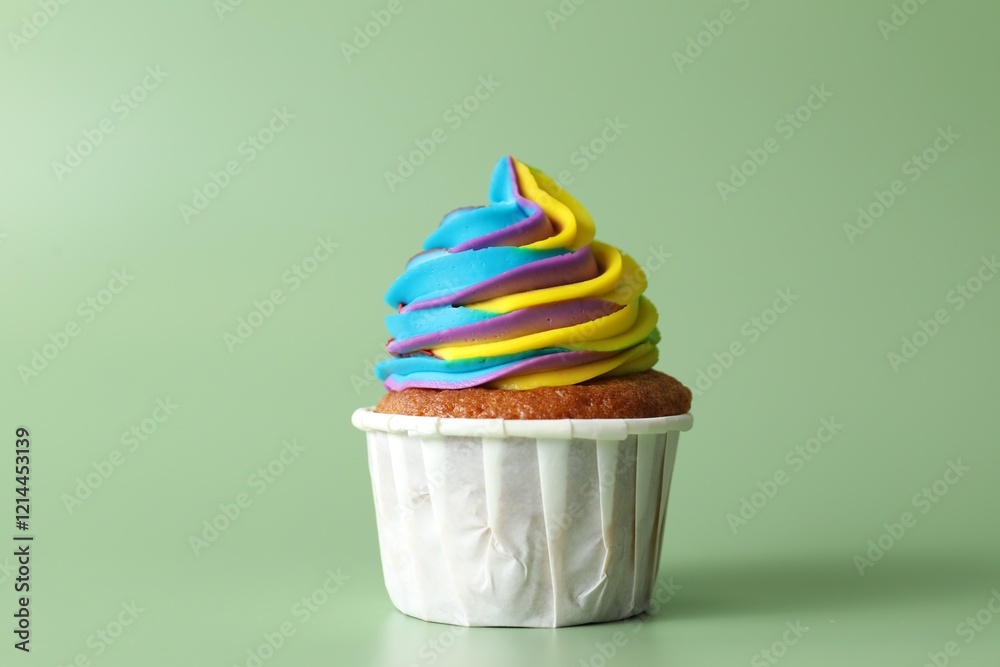 Wall mural Tasty cupcake with colorful cream on light green background, closeup