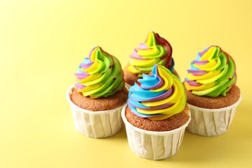 Tasty cupcakes with colorful cream on yellow background, closeup