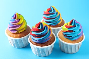 Delicious cupcakes with colorful cream on light blue background, closeup