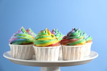 Delicious cupcakes with colorful cream on stand against blue background, closeup