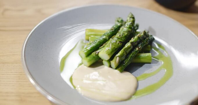 Grilled asparagus served in restaurant on a plate with sause. Healthy food. Eating with fork and knife