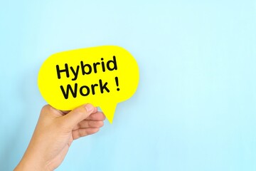 Human hand holding yellow speech bubble with written phrase Hybrid Work. Hiring for hybrid work setup.