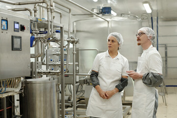 Two workers wearing safety nets and white lab coats observing machinery and equipment in food...