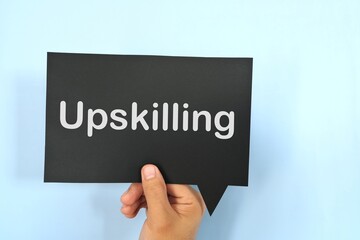 Human hand holding black speech bubble with written phrase Upskilling. Upskilling in workplace.